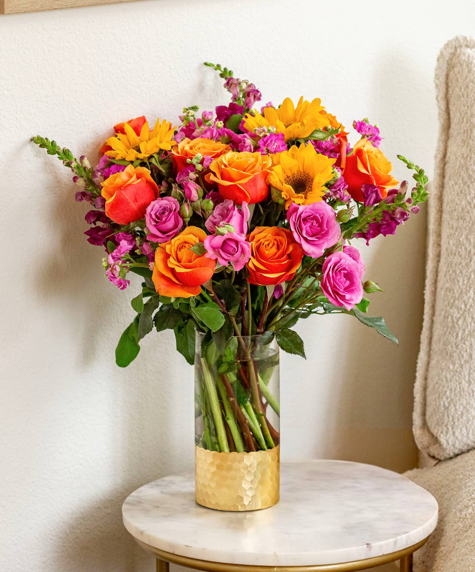 Vibrant floral arrangement with orange roses, pink blooms, and cheerful sunflowers in a vase.