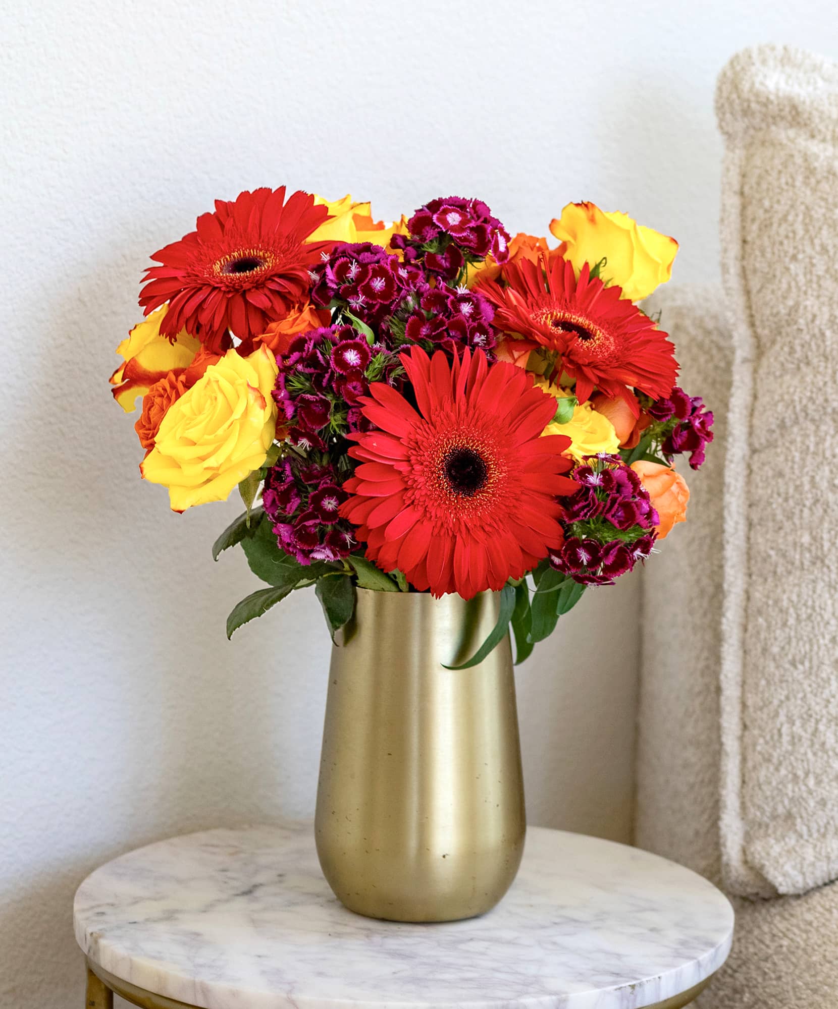 Bright bouquet featuring red gerbera daisies, purple blooms, and yellow roses in a chic vase.